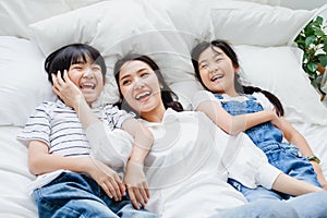 Happy Asian family smiling mother, son & daughter on bed in bedroom. Mom, son & daughter have fun together at home. Love