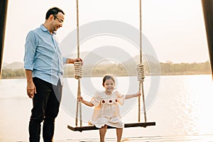 father pushing his cute daughter on a swing and both of them smiling