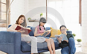 Happy asian family is spending weekend together on couch indoors at home, relaxing and enjoying reading book