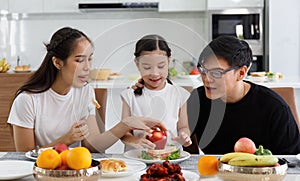 A happy Asian family spends lunch, vegetables, fruit, and dates at the table in their home. Cute little daughter having fun