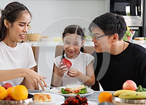 A happy Asian family spends lunch, vegetables, fruit, and dates at the table in their home. Cute little daughter having fun