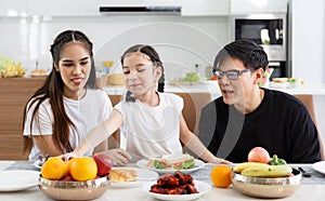 A happy Asian family spends lunch, vegetables, fruit, and dates at the table in their home. Cute little daughter having fun