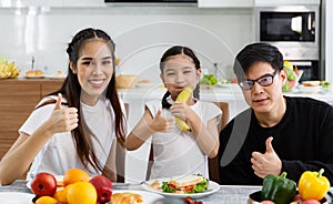 A happy Asian family spends lunch, vegetables, fruit, and dates at the table in their home. Cute little daughter having fun