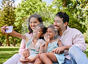 Happy asian family taking selfies and video call while relaxing at the park. Loving parents capturing photos and