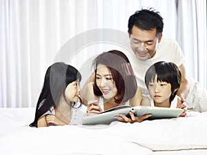 Asian family with two children reading book in bed