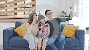 Happy Asian family using smartphone taking a selfie photo together on sofa at home living room