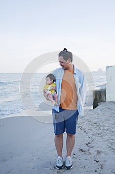 Happy Asian family vacation, a father holds his cute little baby at the beach in summer, he looking at his baby