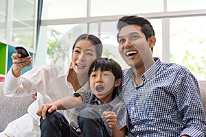 Happy asian family watching tv together on sofa in living room. family and home concept.