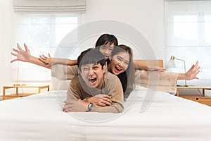 Happy Asian family, young father, mother, cute daughter lying together on bed in bedroom at home. Little girl having fun playing