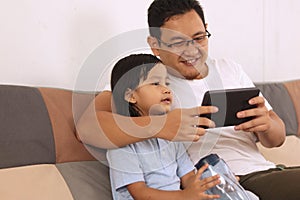 Happy Asian father and baby girl daughter looking at tablet mobile phone, family enjoys quality time