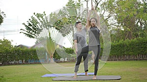 Happy asian father doing training exercises to mother on yoga mat in grass park at the day time