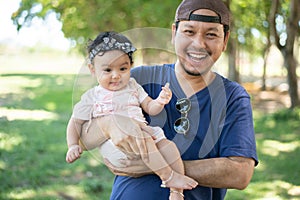 Happy Asian father holding a cute little baby girl on blured background of green garden,  father looking at camera