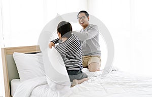 Happy Asian father and little son playing pillow battle on bed in bedroom at home. Weekend Enjoying family leisure morning