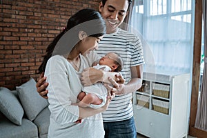 Happy asian father and mother carrying little baby daughter in living room
