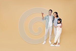 Happy asian father and mother hugging daughter and hand pointing finger isolated on color copy space background. family fun