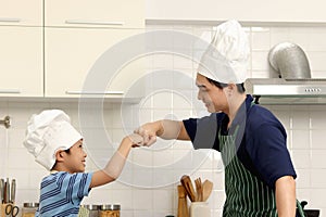 Happy Asian father and son kid with apron chef hat making fist bump during cooking meal at kitchen, cheerful family chef cooking