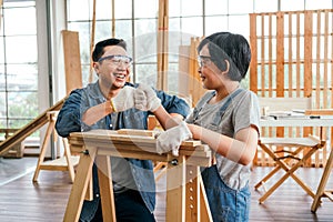 Happy Asian father and son wearing safety glasses and work as a woodworker and carpenter fist bump and smile together.