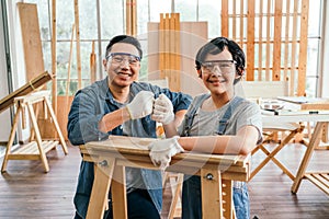Happy Asian father and son wearing safety glasses and work as a woodworker and carpenter fist bump and smile together.