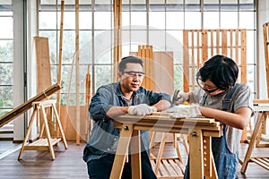 Happy Asian father and son work as a woodworker and carpenter. Father teaching his son to hammer nails on a wooden plank carefully