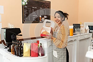 Happy asian female baker holding basket of bread, working at her bakery store. Middle aged female entrepreneur selling homemade