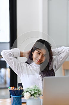 Happy asian female office worker relaxing at office desk.