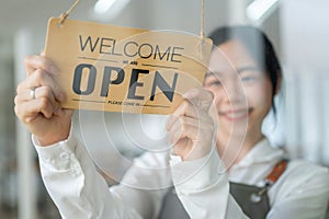 A happy Asian female restaurant staff or waitress is hanging an open sign on the entrance door