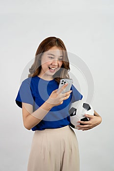 Happy Asian female soccer fan in blue shirt cheering for favorite team with soccer ball, isolated on white background,