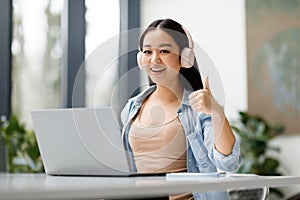 Happy asian female student recommending online studying course, showing thumb up and smiling at camera