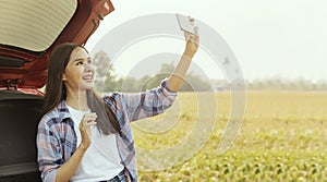 Happy Asian female tourist taking a selfie standing behind a car. photo