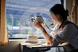 A happy Asian female traveler sits at her seat and takes a picture from the train with her camera