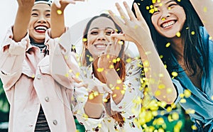 Happy Asian friends having fun throwing confetti outdoor - Young trendy people celebrating at festival event outside