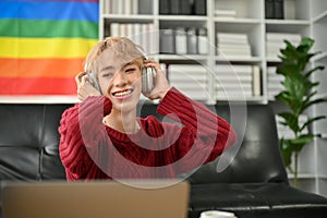 A happy Asian gay man is enjoying the music while relaxing in his apartment living room