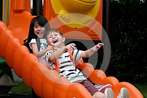 Happy asian girl and caucasian boy playing slide at school, Pre school kids at playground with happiness, Kindergarten children in