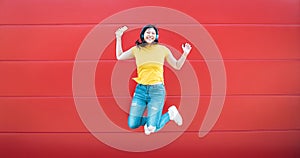 Happy Asian girl jumping while listening music outdoor - Crazy Chinese woman having fun dancing a song against red background