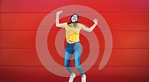 Happy Asian girl jumping while listening music playlist with wireless headphones - Young woman having fun dancing outdoor