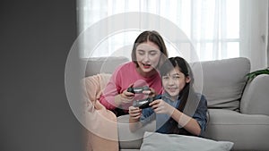 Happy asian girl playing game and sitting while mother lie on sofa. Pedagogy.