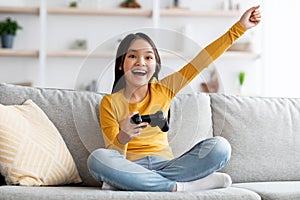 Happy asian girl playing handheld video game at home