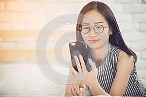 Happy asian girl reading smart phone with smile face on bed .
