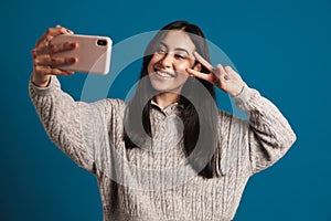 Happy asian girl showing peace sign while taking selfie on smartphone