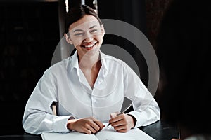 Happy asian girl sitting at table wearing white shirt takes job interview from woman in office