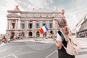 Asian girl traveler with french flag near the main Facade of the Opera Garnier in the historic building of the Academy of