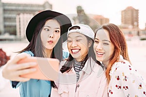 Happy Asian girls taking selfie with mobile smartphone outdoor - Young playful social friends having fun