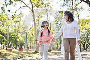 Happy Asian grandmother holding her granddaughter`s hand while walking in the park together