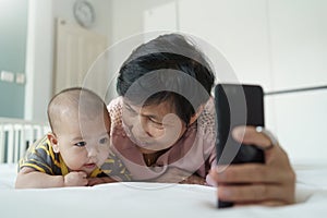 Happy Asian Grandmother and little baby boy or Grandchild playing and taking selfie photos with smartphone together