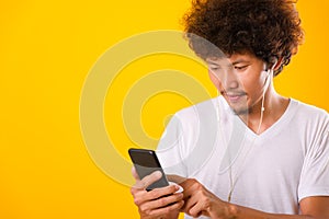 Happy asian handsome man with curly hair he smiling enjoying listening to music on earphones using a mobile smartphone