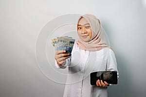 Happy Asian hijab woman excited holding money banknotes and a wallet looking at camera isolated on white background