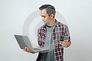 Happy asian indonesian man holding smartphone and laptop computer on isolated background