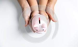 Happy Asian kid and mom saving money together, putting cash into piggy bank. Mother playing with child on heating floor at home,