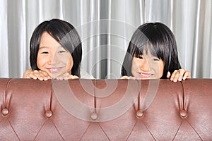 Happy asian kids peeking a sofa