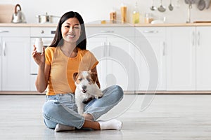 Happy asian lady with cute doggy showing pets supplement jar